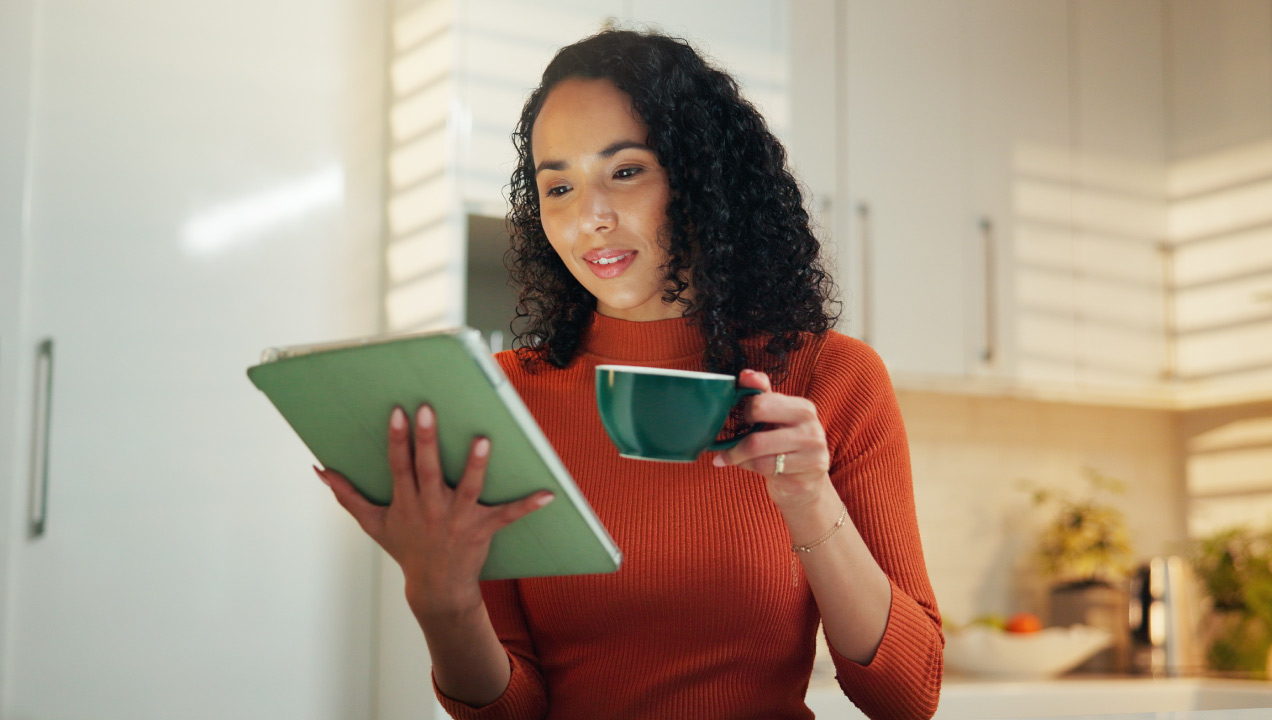 Senhora jovem de pé a ler uma informação no tablet enquanto bebe café